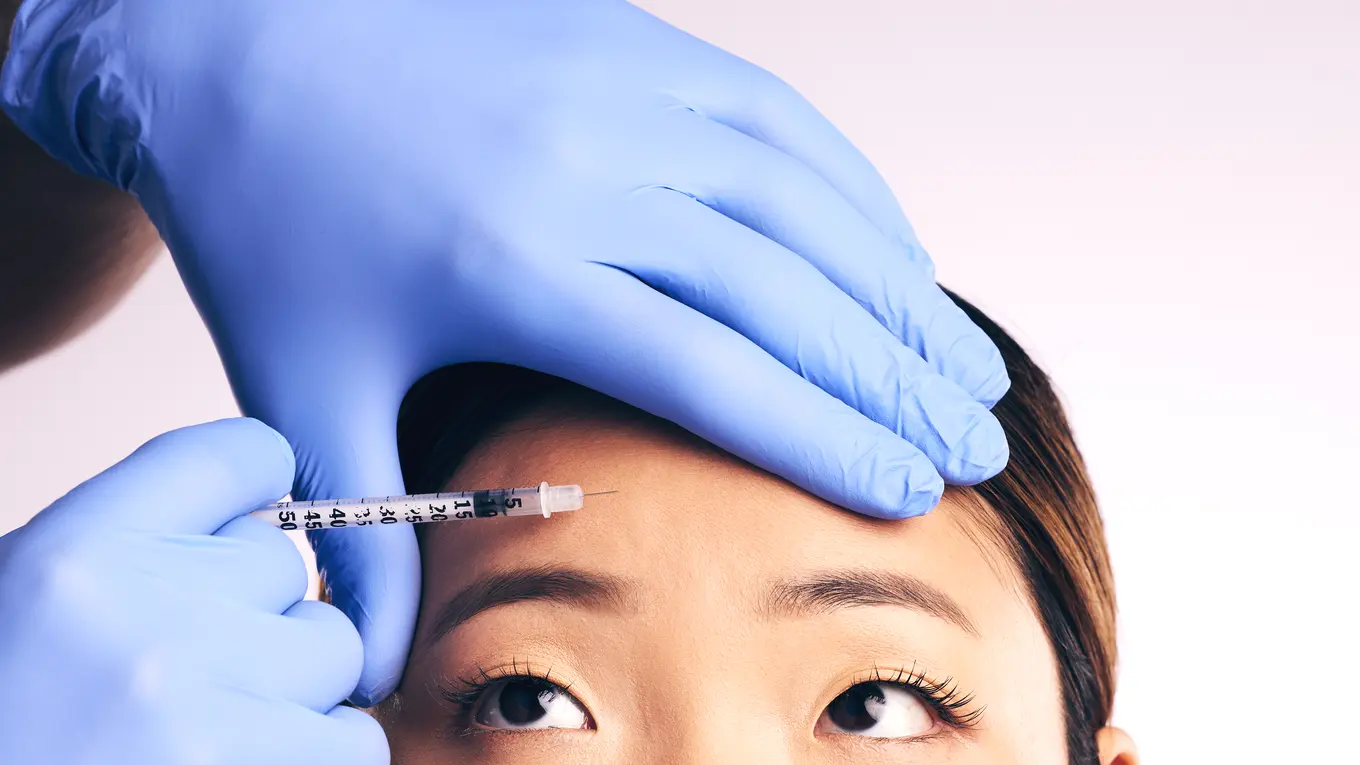 Gloved hand giving forehead injection to woman