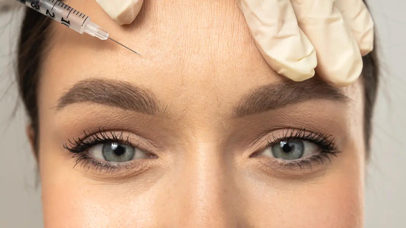 Gloved hand giving forehead injection to woman