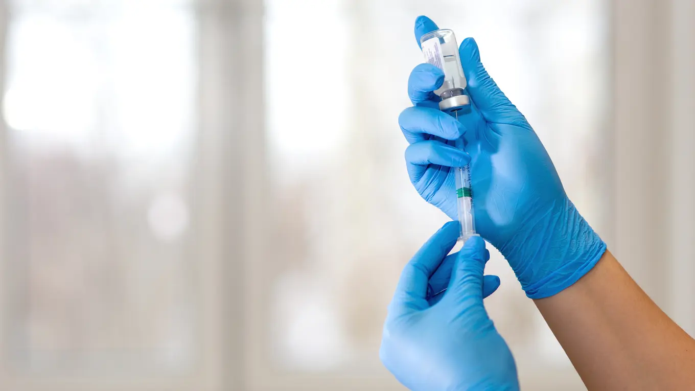 Hands in blue gloves preparing syringe with vial