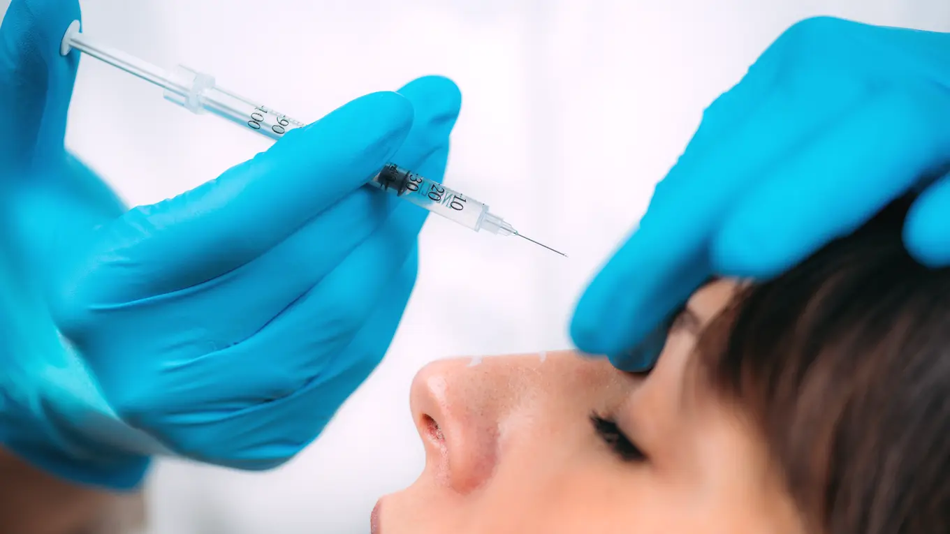 Gloved hands giving facial injection with syringe