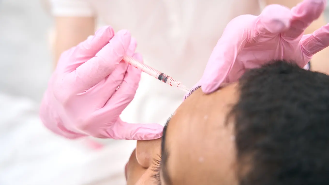 Doctor injecting filler into forehead with pink gloves