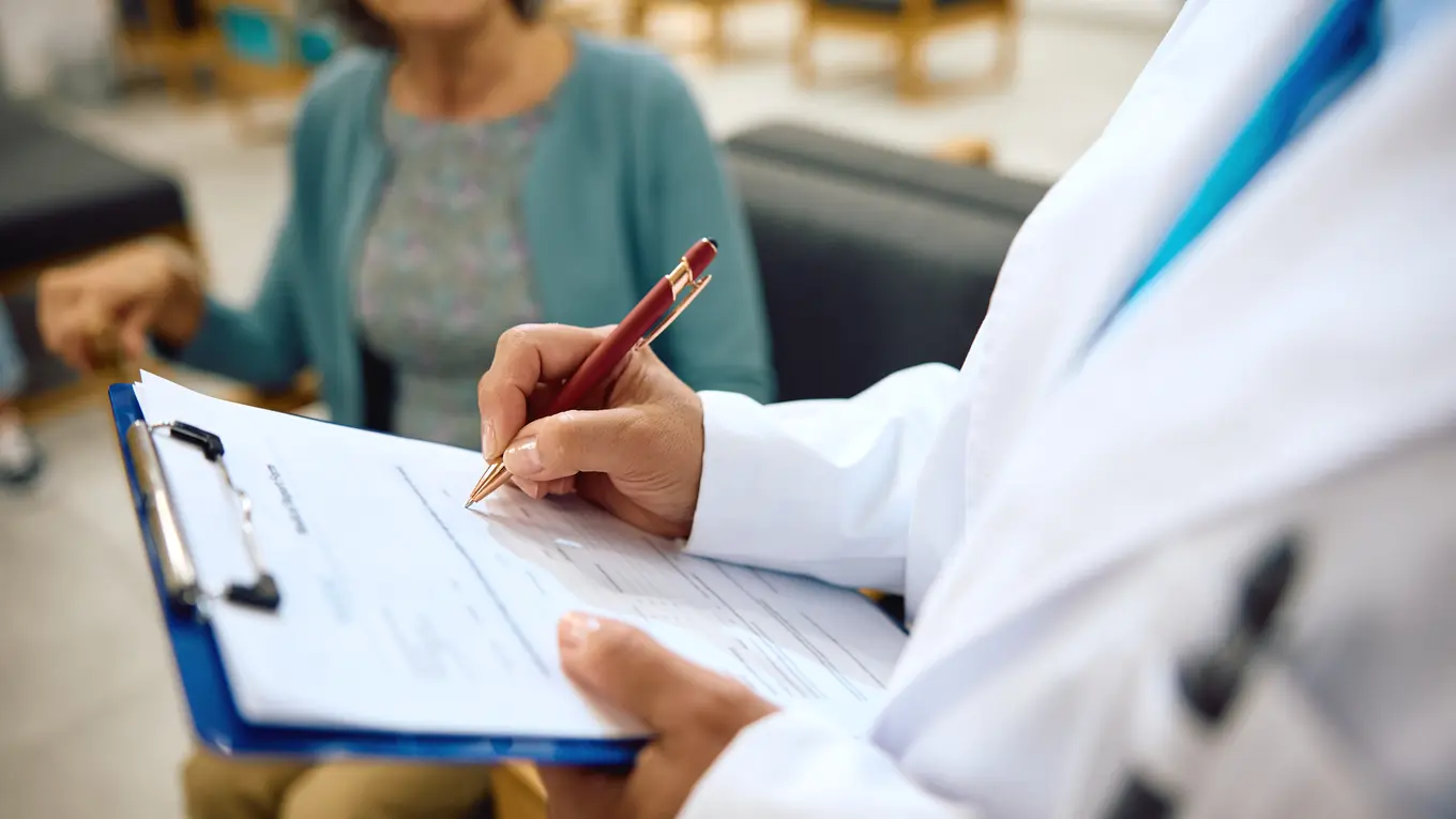 Doctor writing on clipboard with patient in background