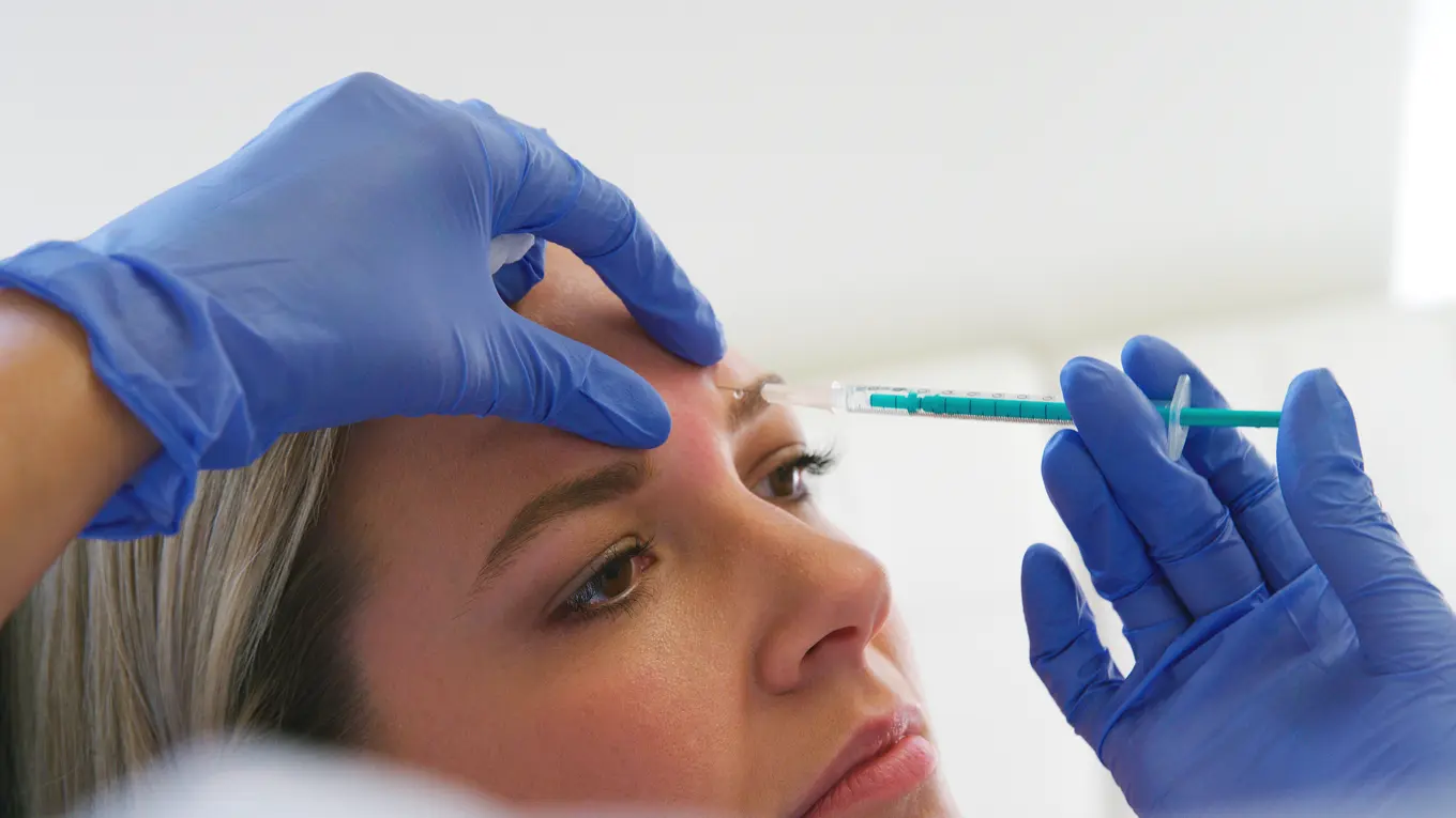 Gloved hands giving forehead injection with syringe