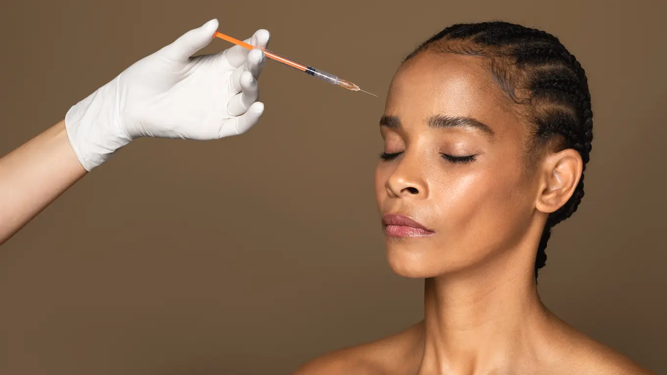 Gloved hand administering facial injection to woman