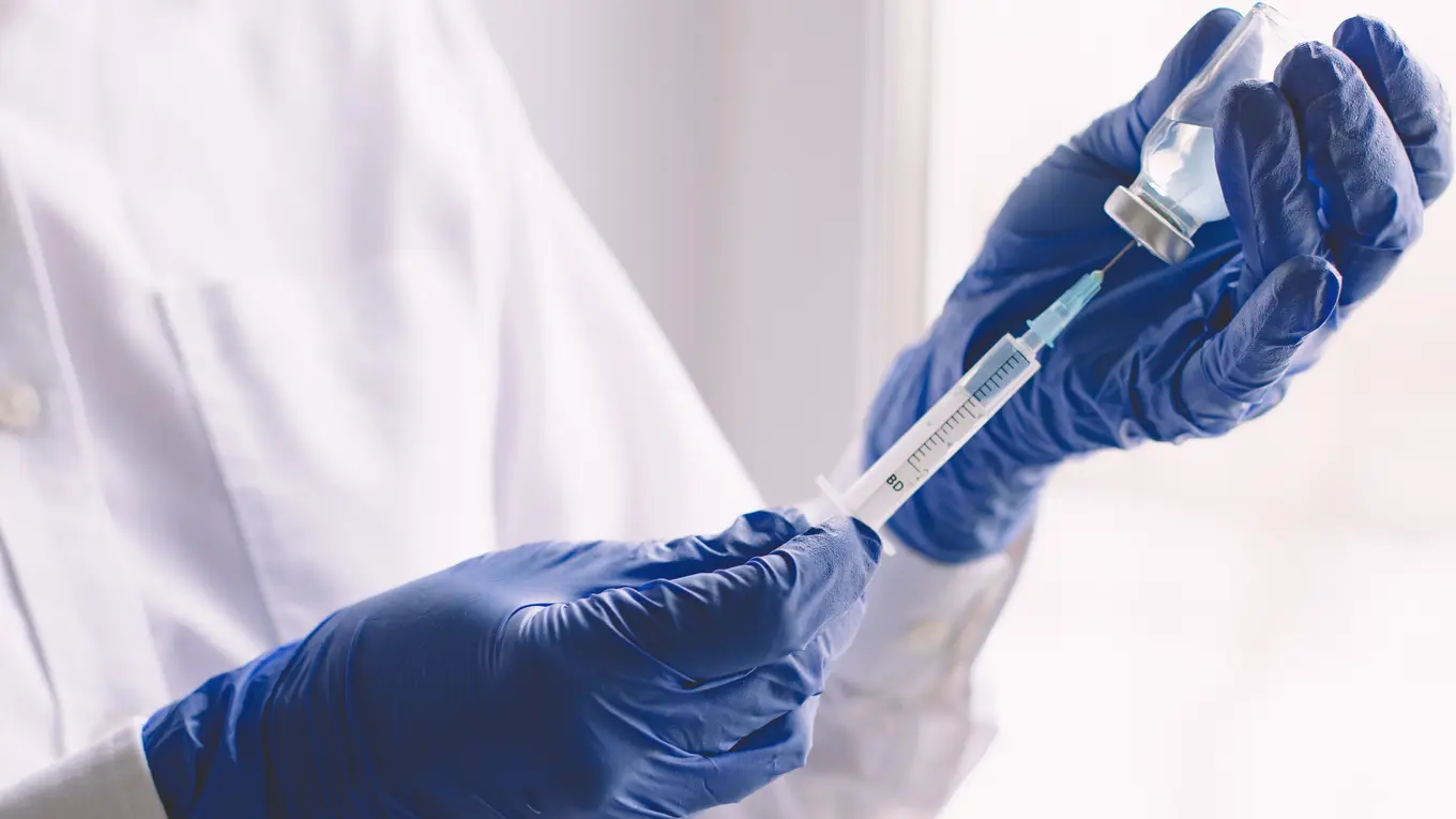Hands in blue gloves preparing syringe with vial
