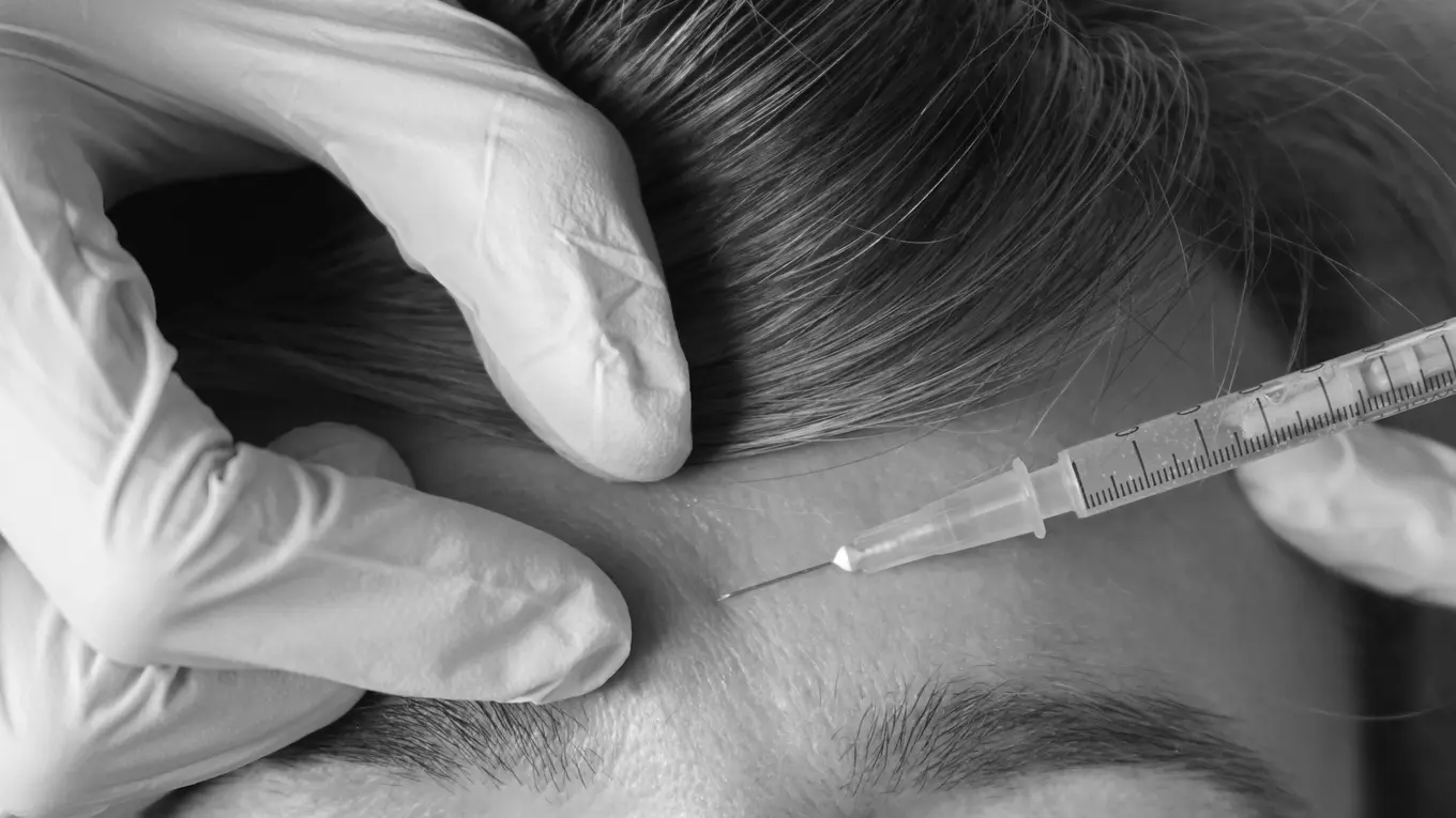 Gloved hand administering facial injection with syringe
