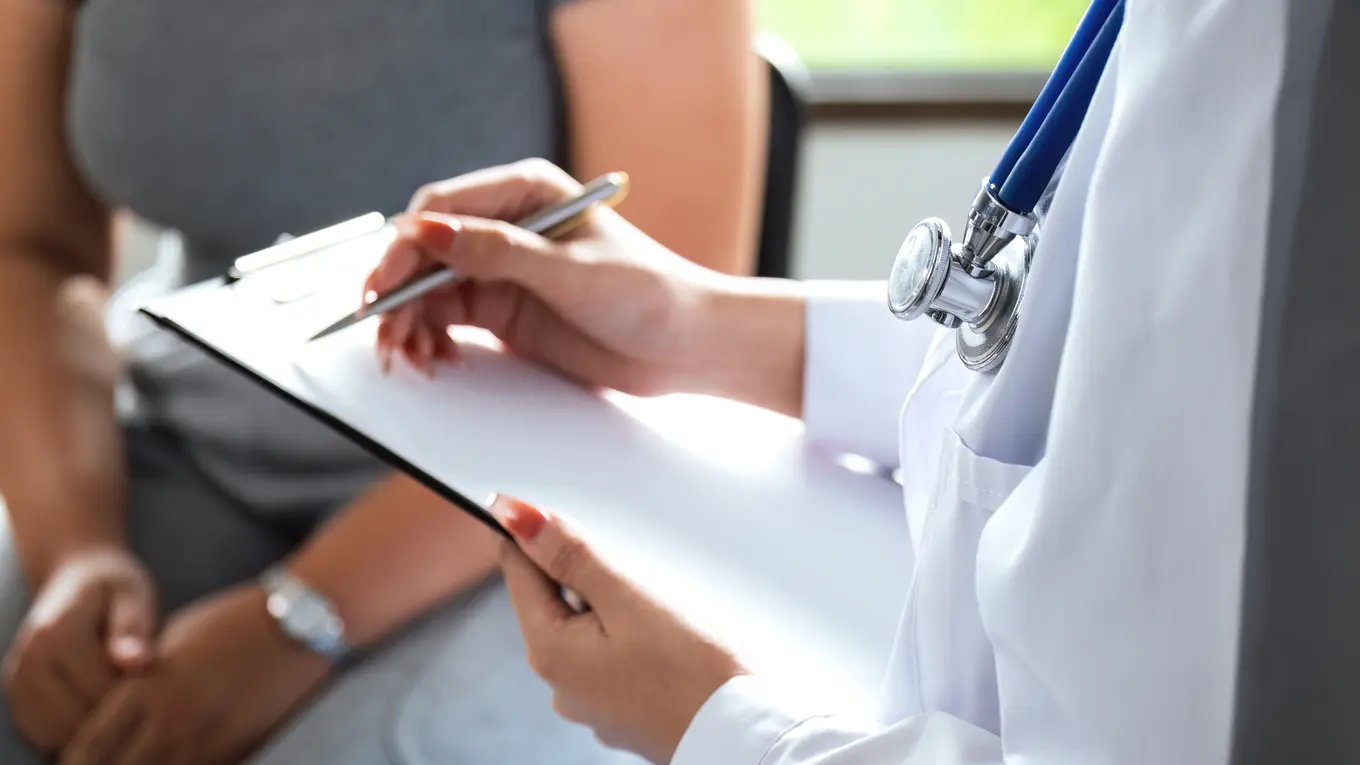 Doctor writing on clipboard with patient in background